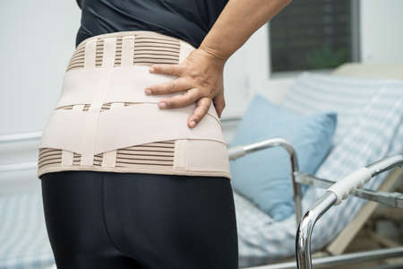 Asian lady patient wearing back pain support belt for orthopedic lumbar with walker.