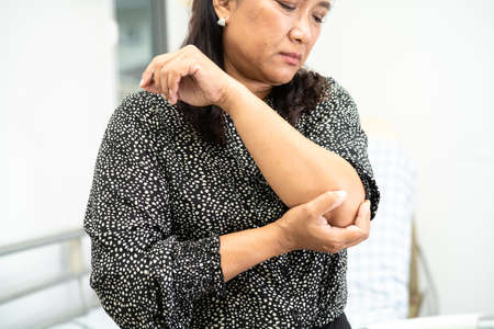 Asian lady woman patient touch and feel pain her elbow and arm, healthy medical concept.