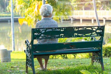 Asian elderly woman depressed and sad sitting back on bench in autumn park.の写真素材