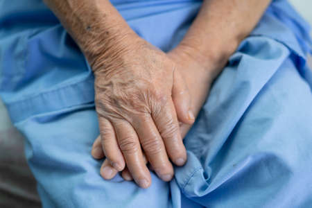 Asian senior or elderly old lady woman patient hold her hand with hope while sitting on bed in...
