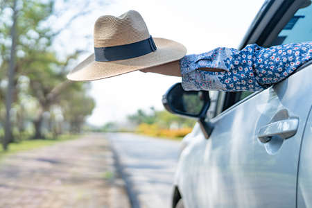Happy enjoy and freedom in traveling trip with raised hand and holding beautiful hat outside of window car in summer vacation holidayの写真素材