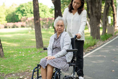 Caregiver help and care Asian senior or elderly old lady woman patient sitting and happy on wheelchair in park, healthy strong medical concept.の写真素材