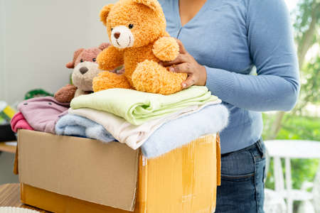 Holding clothing donation box with used clothes and doll at home to support help for poor people in the world.の写真素材