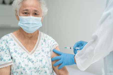 Elderly Asian senior woman wearing face mask getting covid-19 or coronavirus vaccine by doctor make injection.の写真素材