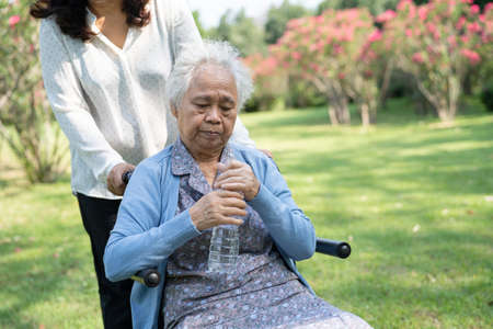 Caregiver help and care Asian senior or elderly old lady woman patient sitting on wheelchair and drink water in park.の写真素材