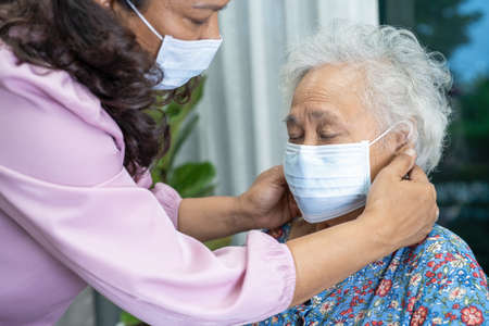 Caregiver help Asian senior or elderly old lady woman sitting on wheelchair and wearing a face mask for protect safety infection Covid 19 Coronavirus.の写真素材