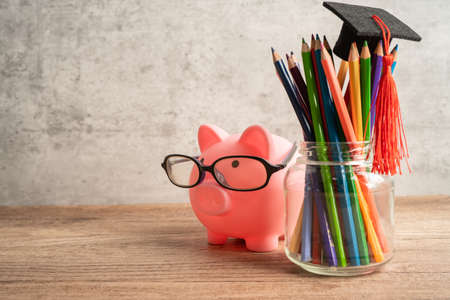 Pigging bank wearing eyeglass with colorful pencils; saving bank education concept.