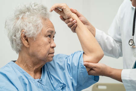 Asian senior or elderly old lady woman patient feel pain her elbow on bed in nursing hospital ward, healthy strong medical concept.の写真素材