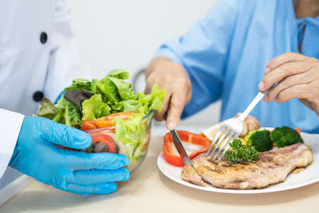 Asian senior or elderly old lady woman patient eating breakfast and vegetable healthy food with hope and happy while sitting and hungry on bed in hospital.の写真素材