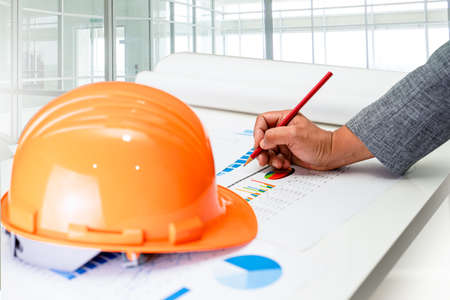 Asian engineer with architectural house plan project blueprint, graph and yellow helmet and engineering construction tools.の写真素材