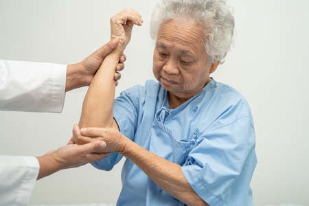 Asian senior or elderly old lady woman patient feel pain her elbow on bed in nursing hospital ward,...