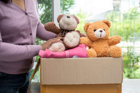 Holding clothing donation box with used clothes and doll at home to support help for poor people in the world.の写真素材