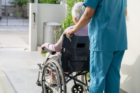 Caregiver help and care Asian senior or elderly old lady woman patient sitting in wheelchair on ramp at nursing hospital, healthy strong medical conceptの写真素材