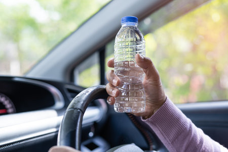 Asian woman driver holding bottle for drink water while driving a car. Plastic hot water bottle cause fire.の写真素材