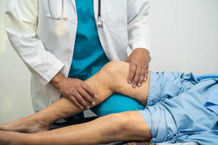 Asian doctor physiotherapist examining, massaging and treatment knee and leg of senior patient in orthopedist medical clinic nurse hospital.の写真素材