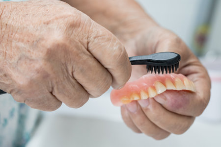Asian senior or elderly old woman patient use toothbrush to clean partial denture of replacement...