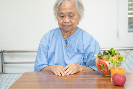 Asian senior or elderly old lady woman patient eating Salmon steak breakfast with vegetable healthy food while sitting and hungry on bed in hospital.の写真素材