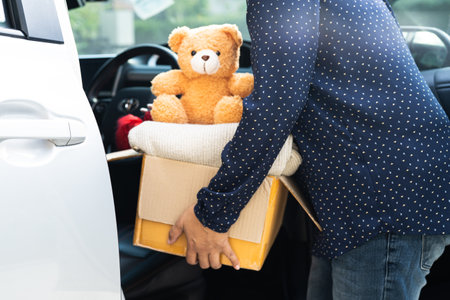 Volunteer woman provide clothing donation box with used clothes and doll in car to support help for refugee, homeless or poor people in the world.の写真素材
