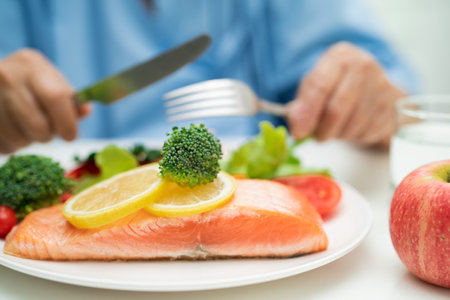 Asian elderly woman patient eating salmon steak breakfast with vegetable healthy food in hospital.の写真素材