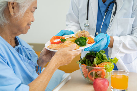 Asian senior woman patient eating Salmon steak breakfast with vegetable healthy food while sitting and hungry on bed in hospital.の写真素材