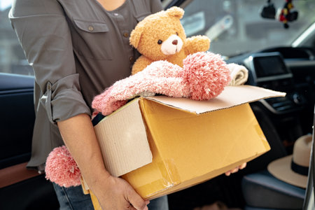Volunteer woman provide clothing donation box with used clothes and doll in car to support help for refugee, homeless or poor people in the world.の写真素材