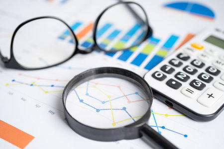 Eyeglass with calculator on chart graph paper. Finance, account, statistic, investment data economy,...