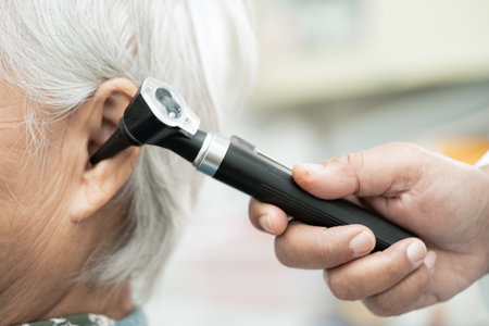 Audiologist or ENT doctor use otoscope checking ear of asian senior woman patient treating hearing...