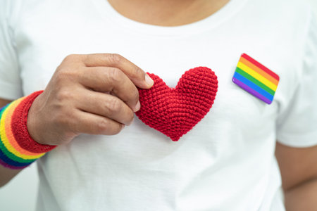 Asian lady wearing rainbow flag wristbands and hold heart, symbol of LGBT pride month celebrate...