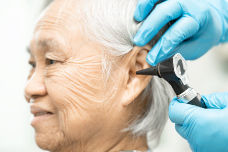 Audiologist or ENT doctor use otoscope checking ear of asian senior woman patient treating hearing loss problem.の写真素材