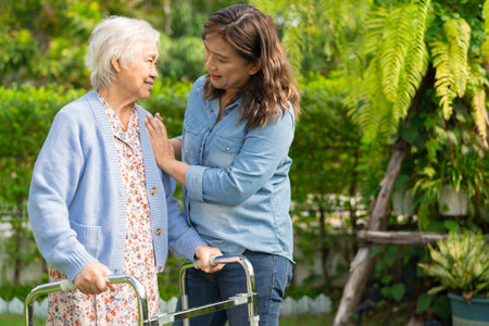 Doctor caregiver help and care Asian senior woman patient walk with walker in park at hospital.の写真素材