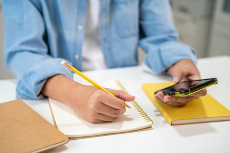 Teenage write in notebook and use mobile phone search data online to online learning university education.の写真素材