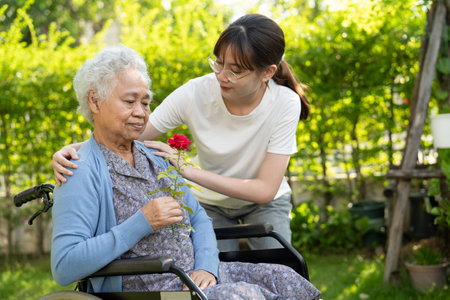 Asian elderly woman holding red rose flower, smile and happy in the sunny garden.の写真素材