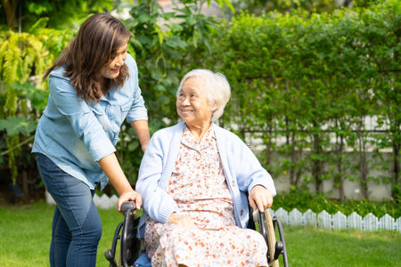 Caregiver helping and caring for an elderly woman patient sitting on a wheelchair at a nursing hospital ward.の写真素材