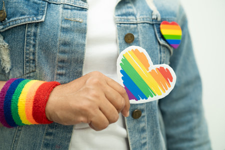Asian lady wearing rainbow flag wristbands and hold red heart, symbol of LGBT pride month