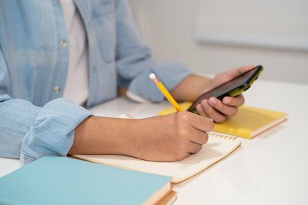 Teenage write in notebook and use mobile phone search data online to online learning university education.の写真素材