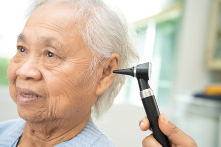 Audiologist or ENT doctor use otoscope checking ear of asian senior woman patient treating hearing loss problem.の写真素材