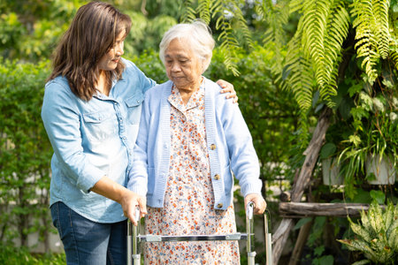 Caregiver help and care Asian senior woman  walk with walker at park.の写真素材