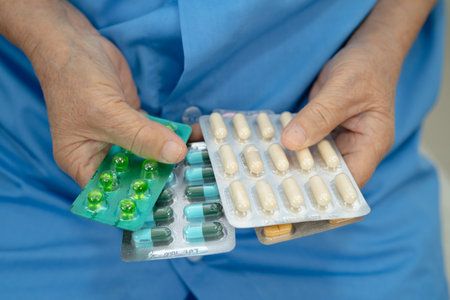 Asian senior woman patient holding antibiotics capsule pills  for treatment infection patient in...