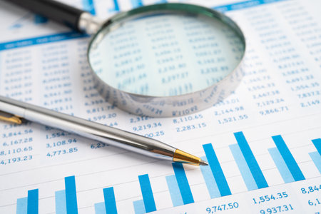 Magnifying glass on spreadsheet and graph paper.
