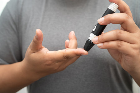 Asian woman self testing to check blood sugar level diabetes by digital lancet on finger at home.