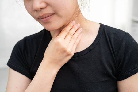 Asian woman touching her neck and throat for thyroid gland problem.