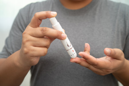 Asian woman self testing to check blood sugar level diabetes by digital lancet on finger at home.の写真素材