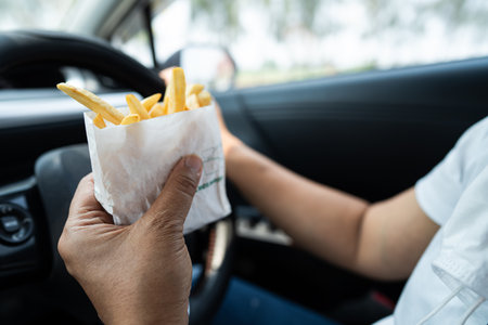 Asian lady holding French fries potato chips to eat in car.