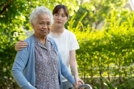 Caregiver help Asian elderly woman patient walk with walker in park, healthy strong medical concept.の写真素材