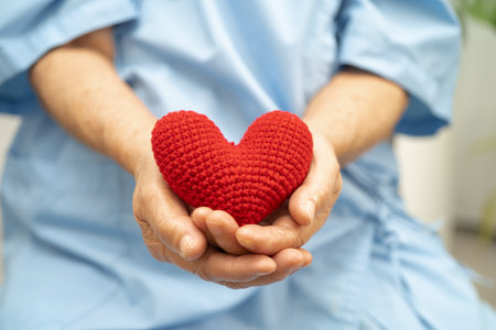Asian senior woman patient holding red heart in hospital.