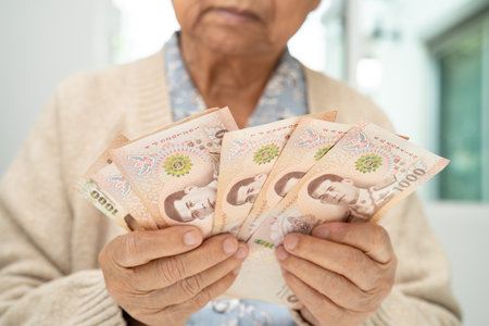 Asian elderly woman holding Thai banknotes money in hand. Poverty, saving problem in retirement.の写真素材