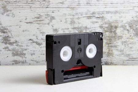 Black mini DV cassette on white table with wooden old wall closeup