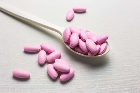 Many pink tablets pills on a spoon on white canvas backgroundの写真素材