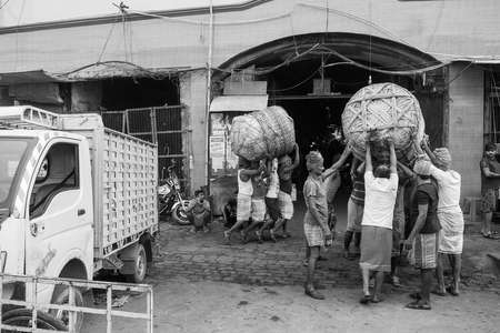 labours picking up a heavy load of goods in Koley Market, Kolkata, India.