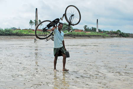 howrah west bengal india on july 6th 2012:People in rural Howrah have to carry bicycles on their shoulders at low tide situation.のeditorial素材